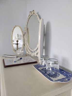 Een kaptafel met twee sierlijke spiegels, een afstandsbediening, een notitieboekje en een glazen pot.