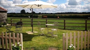 A patio area with outdoor seating, a wooden fence, and a view of a field with cows. - Burton Grange Farmhouse B&B (York)
