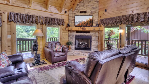 A log cabin interior with a fireplace, leather furniture, and a stone wall. - AMAZING GATED COMMUNITY - YOUR OWN PRIVATE SAUNA & HOT TUB ON BACK PORCH (Sevierville)