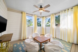 Relax in this serene sunroom with a ceiling fan, comfortable seating, and a large TV.
