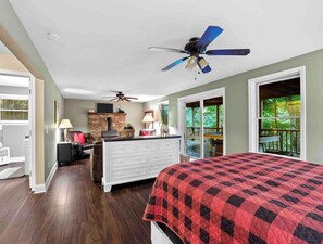 Une chambre à coucher comprenant un lit, une commode, une cheminée, un ventilateur de plafond et un balcon avec vue sur la verdure.