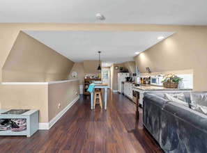 A modern kitchen with white appliances, a dining area with a blue table, and a living room with a grey sofa.