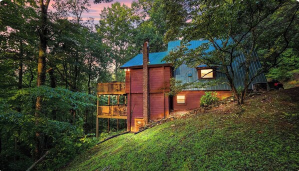 Une cabane dotée d’une terrasse en bois et d’un toit bleu, entourée d’une forêt dense.