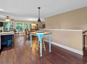 A spacious kitchen with wooden flooring, a dining area with chairs, and a ceiling fan.