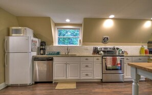 A kitchen with white cabinets, a microwave, a dishwasher, a stove, and a window with a view of trees.