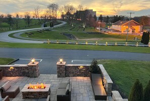 A patio area with stone seating and a fire feature, overlooking a road and a building with lights. - Elegance on The Farm •Limitless Amenities ♦Pool ♦Hot Tub ♦Fish Pond +more! (Ronks)