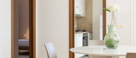 Un espace repas moderne avec une table ronde, des chaises blanches et un vase vert contenant une fleur blanche.