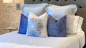 Una cama bien hecha con cabecera gris, ropa de cama blanca y almohadas con estampado azul.