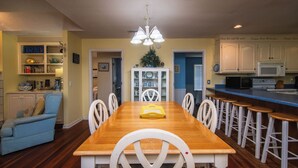 Un comedor con mesa de madera y sillas blancas, un sofá azul, y una cocina con armarios blancos y un microondas.
