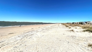 Ein Strand mit blauem Himmel, sandigem Ufer und einigen Spaziergängern.