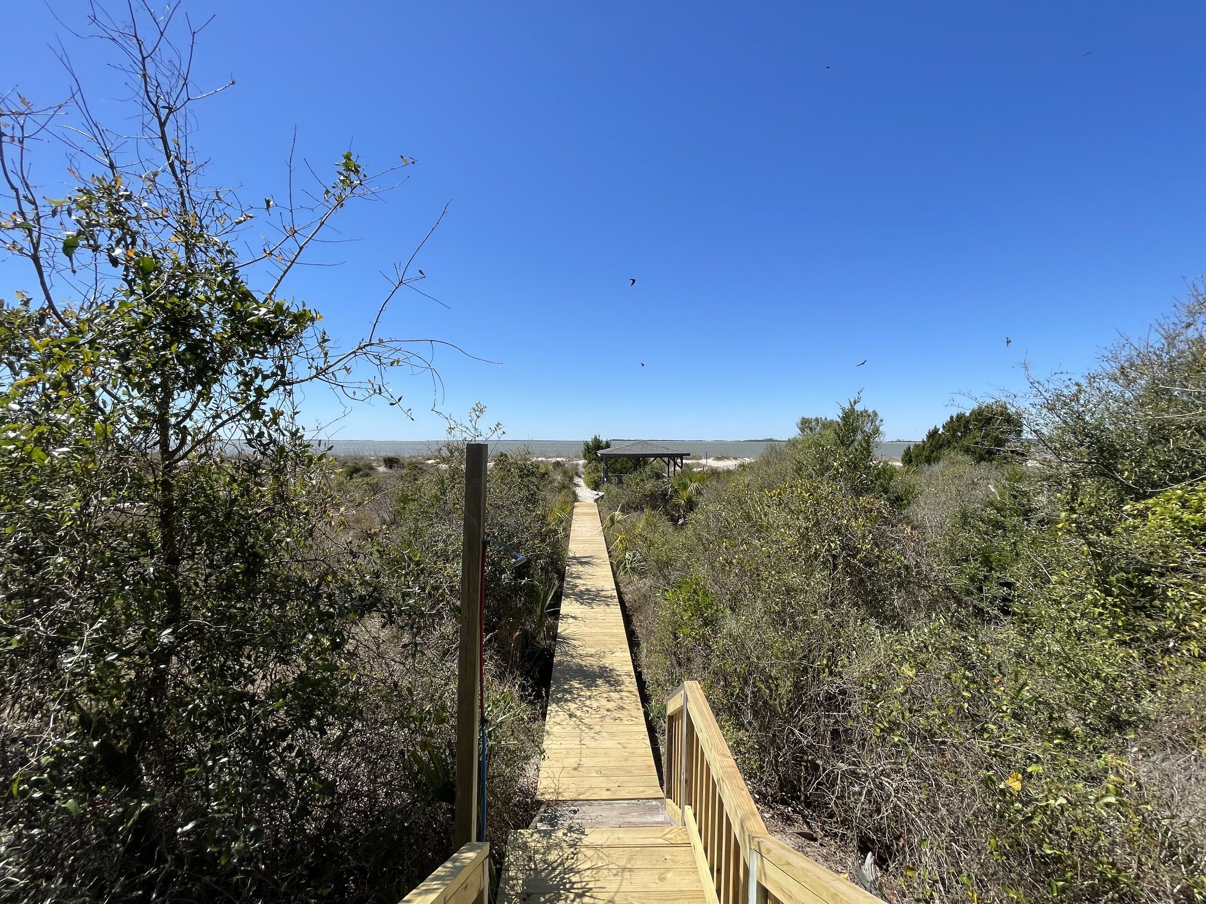 A wooden boardwalk leading to a covered structure in a natural setting with dense vegetation.