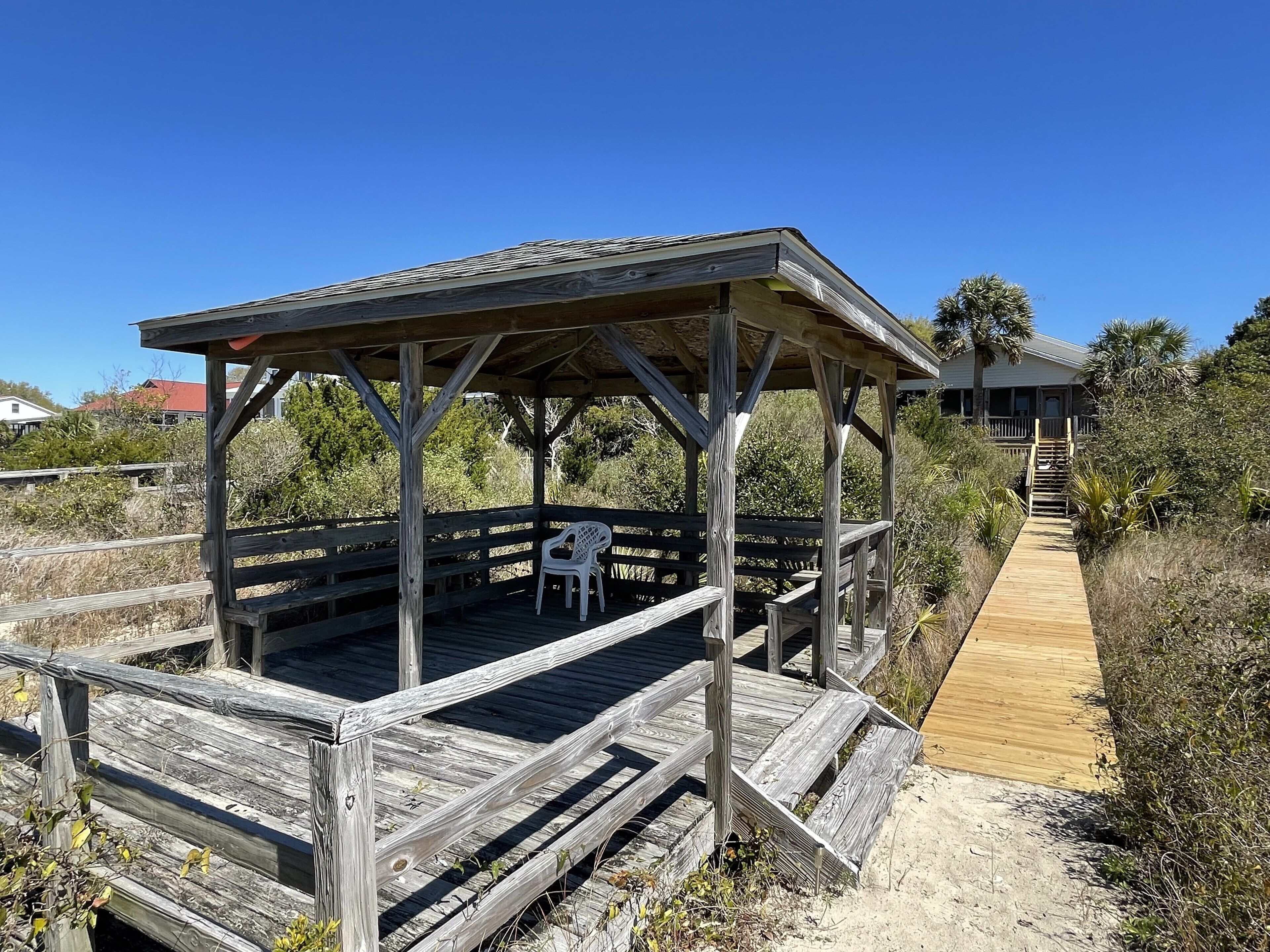 A wooden gazebo with a bench and a pathway leading to a house.