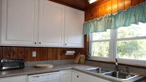 Eine Küche mit Holzschränken, einem Toaster, einem Geschirrspüler und einem Fenster mit Vorhang.