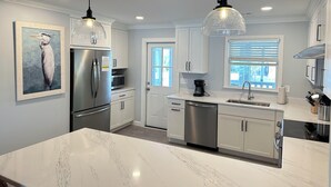 Uma cozinha moderna com armários brancos, eletrodomésticos de aço inoxidável e iluminação pendente.