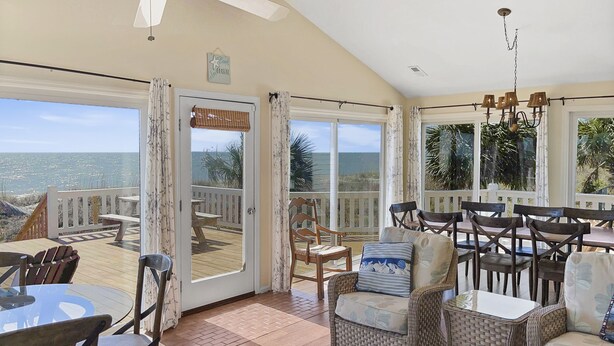 Quarto espaçoso com uma grande porta de vidro deslizante que dá para um deck com vista para o oceano. No interior, há cadeiras de vime e uma mesa, além de um lustre pendurado no teto.