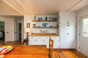 Uma cozinha com prateleiras de madeira, uma mesa, cadeiras e uma geladeira.