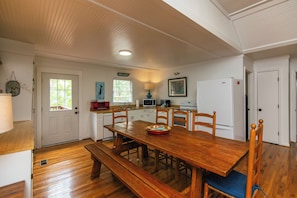 Un coin repas avec une table en bois, des bancs et des chaises. On y trouve également un four à micro-ondes, un réfrigérateur et une fenêtre donnant sur un paysage verdoyant.
