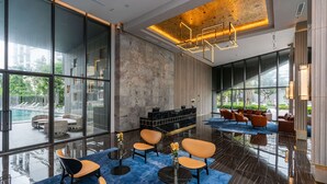 A modern lobby with large windows, a pool view, and a seating area with sofas and tables.