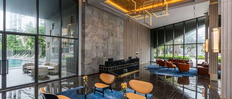 En moderne lobby med store vinduer, udsigt til poolen og et loungeområde med sofaer og borde.
