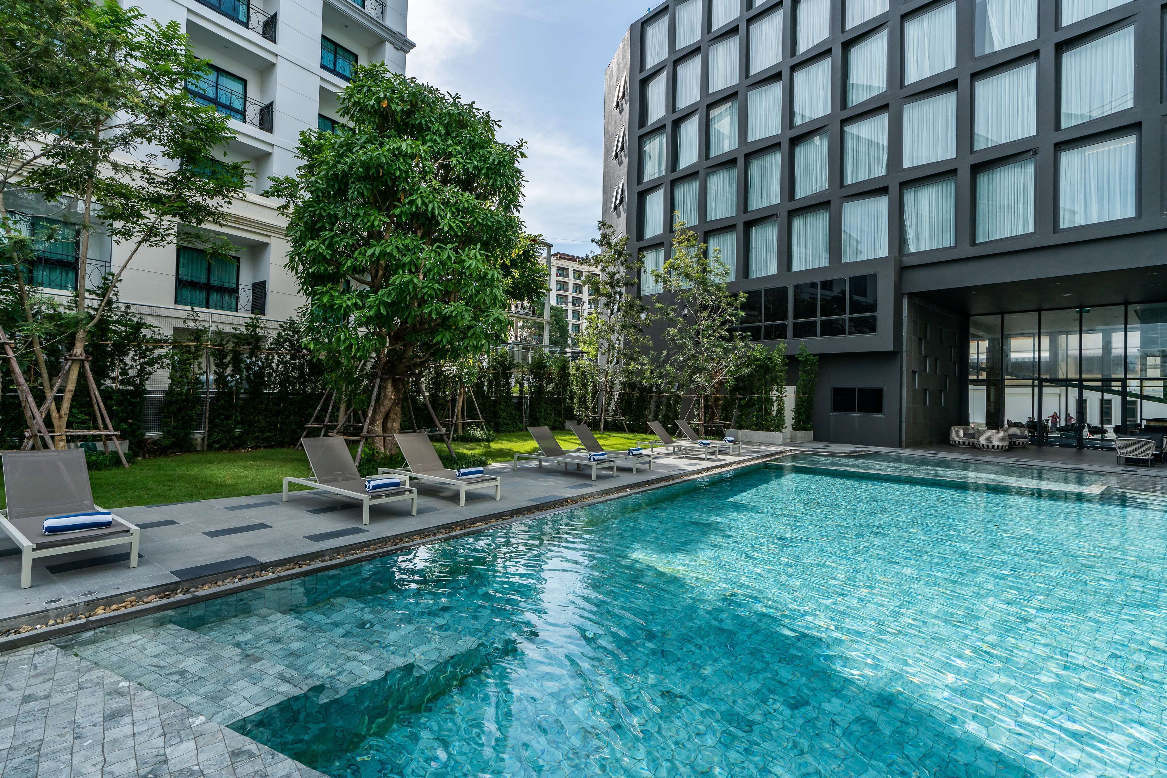 A modern hotel with a swimming pool, lounge chairs, and a well-maintained garden.