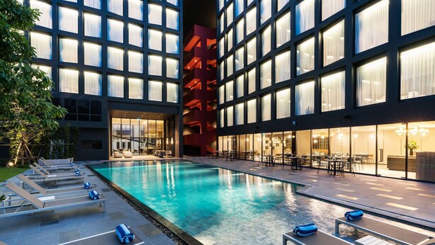 A modern hotel with a large indoor pool, sun loungers, and a dining area with tables and chairs.