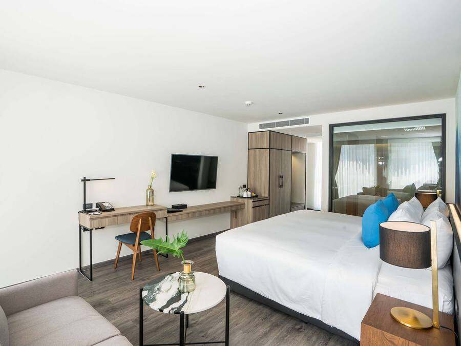 A modern hotel room with a bed, a desk, a chair, a TV, and a window with curtains.