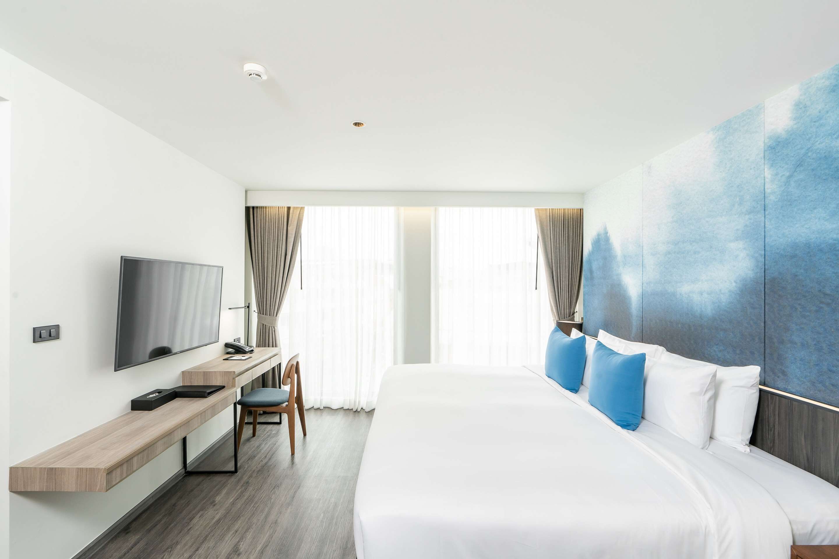Una habitación de hotel moderna con una cama grande, un escritorio y un televisor de pantalla plana, y una ventana con cortinas.