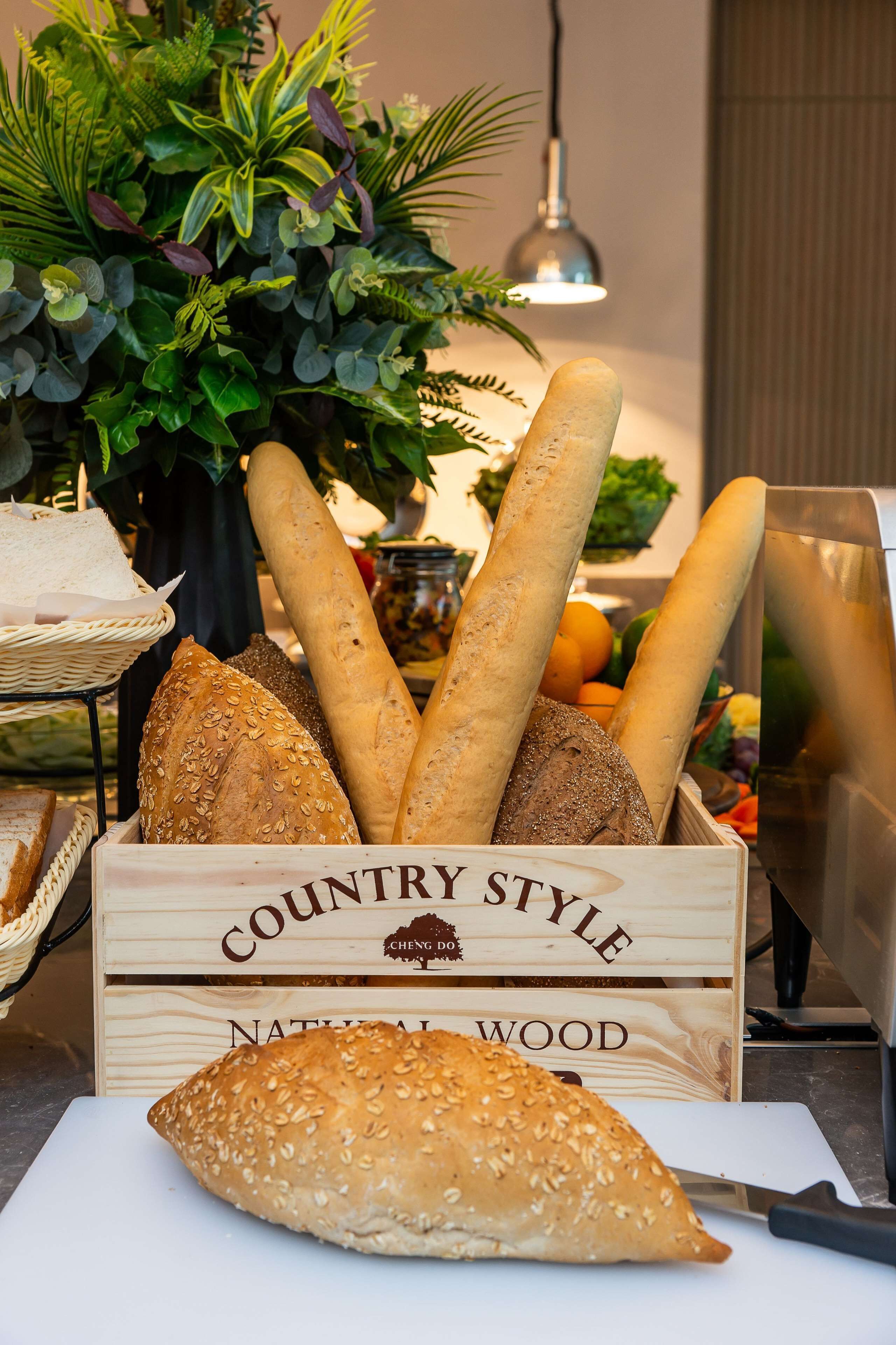 A wooden crate labeled "Country Style" filled with various breads and a cutting board with a knife.