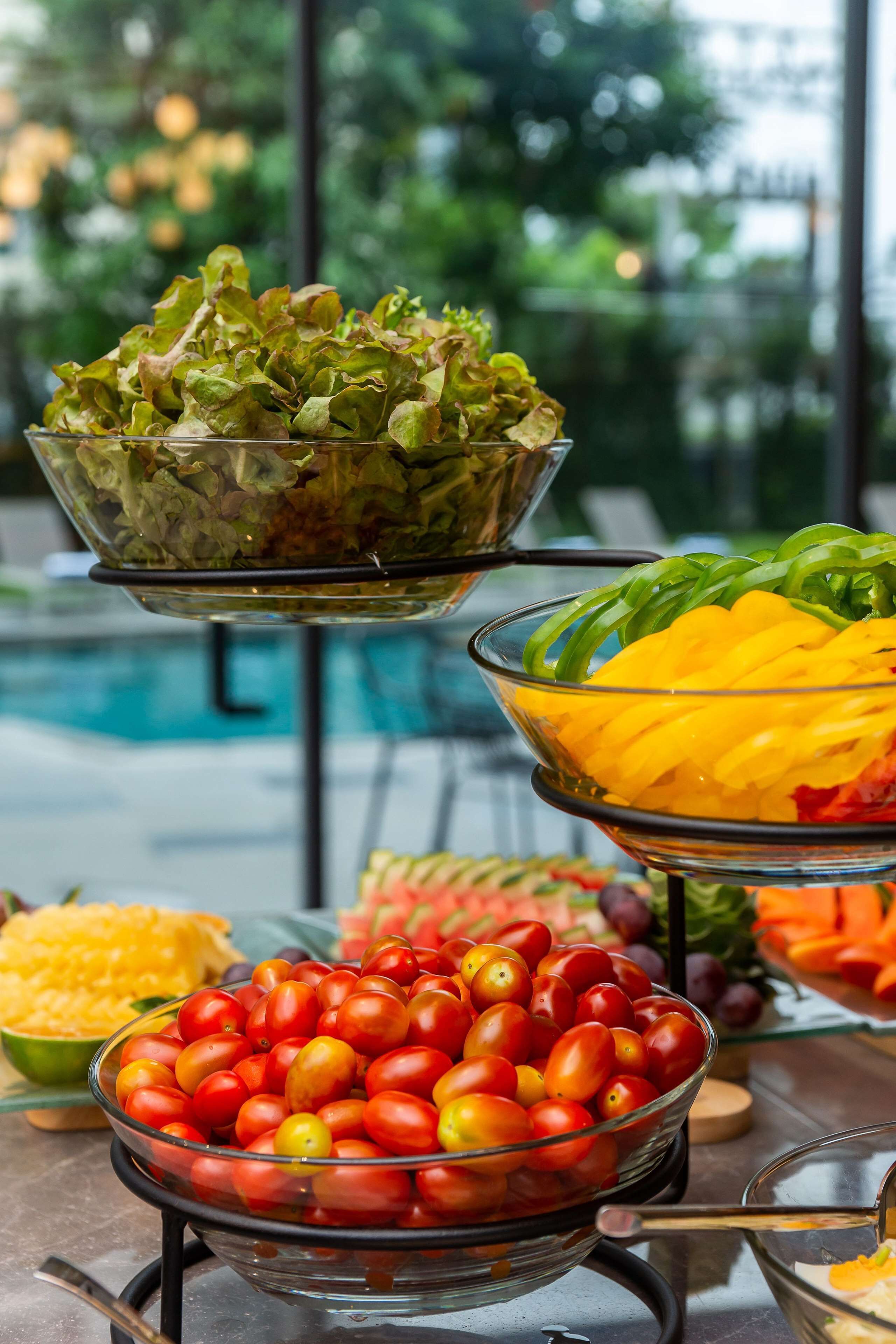 Un bufé con diversos alimentos, entre ellos ensaladas, frutas y tomates.