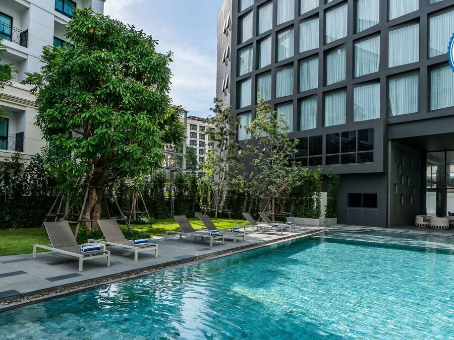 A modern hotel with a swimming pool, lounge chairs, and a large building with a SHA certification badge.