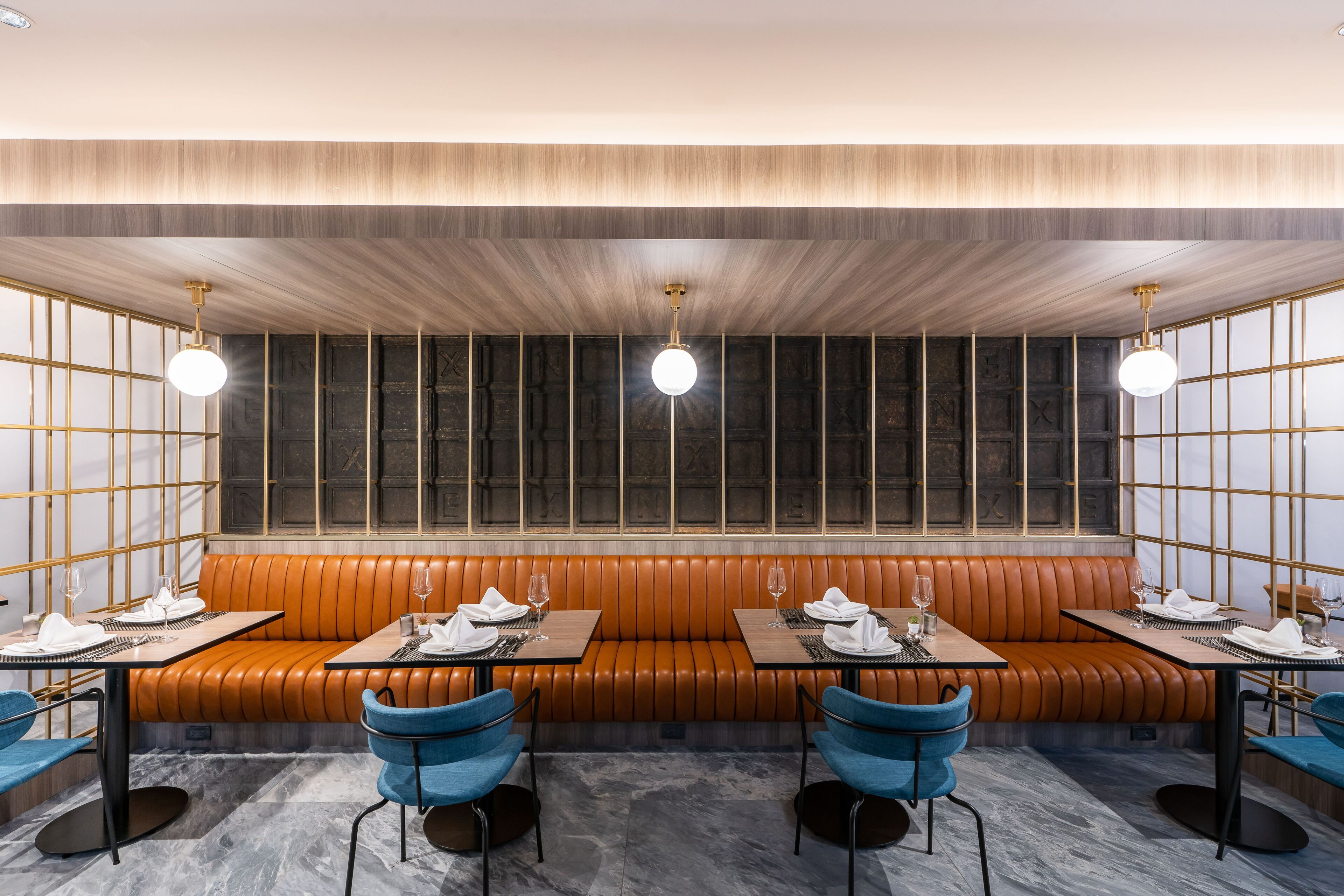 Un restaurante con una larga zona de asientos en banco de madera, suelo de mármol y sillas azules.