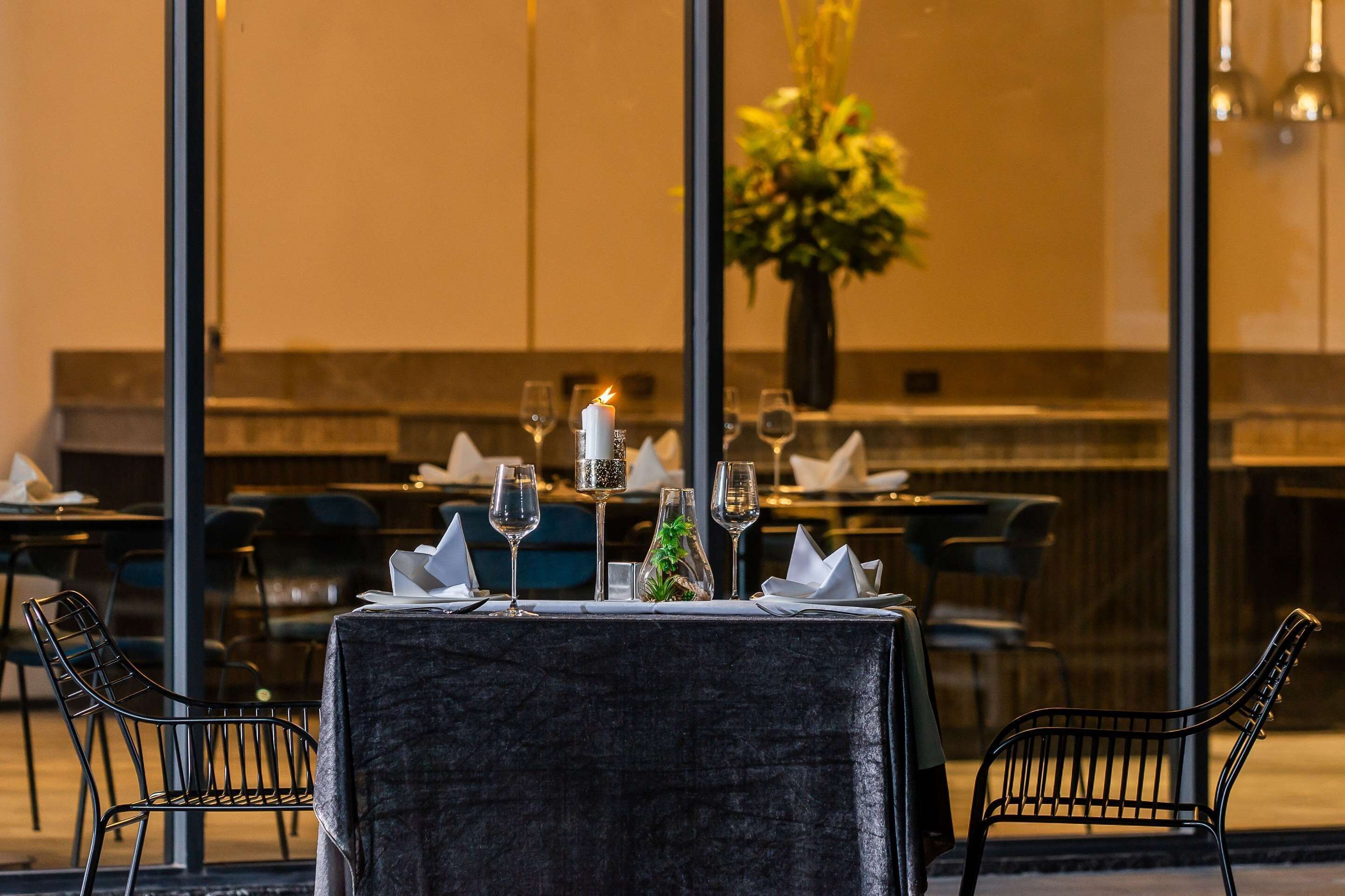 A dining table set with glasses, a candle, and a vase with flowers, with chairs around it.