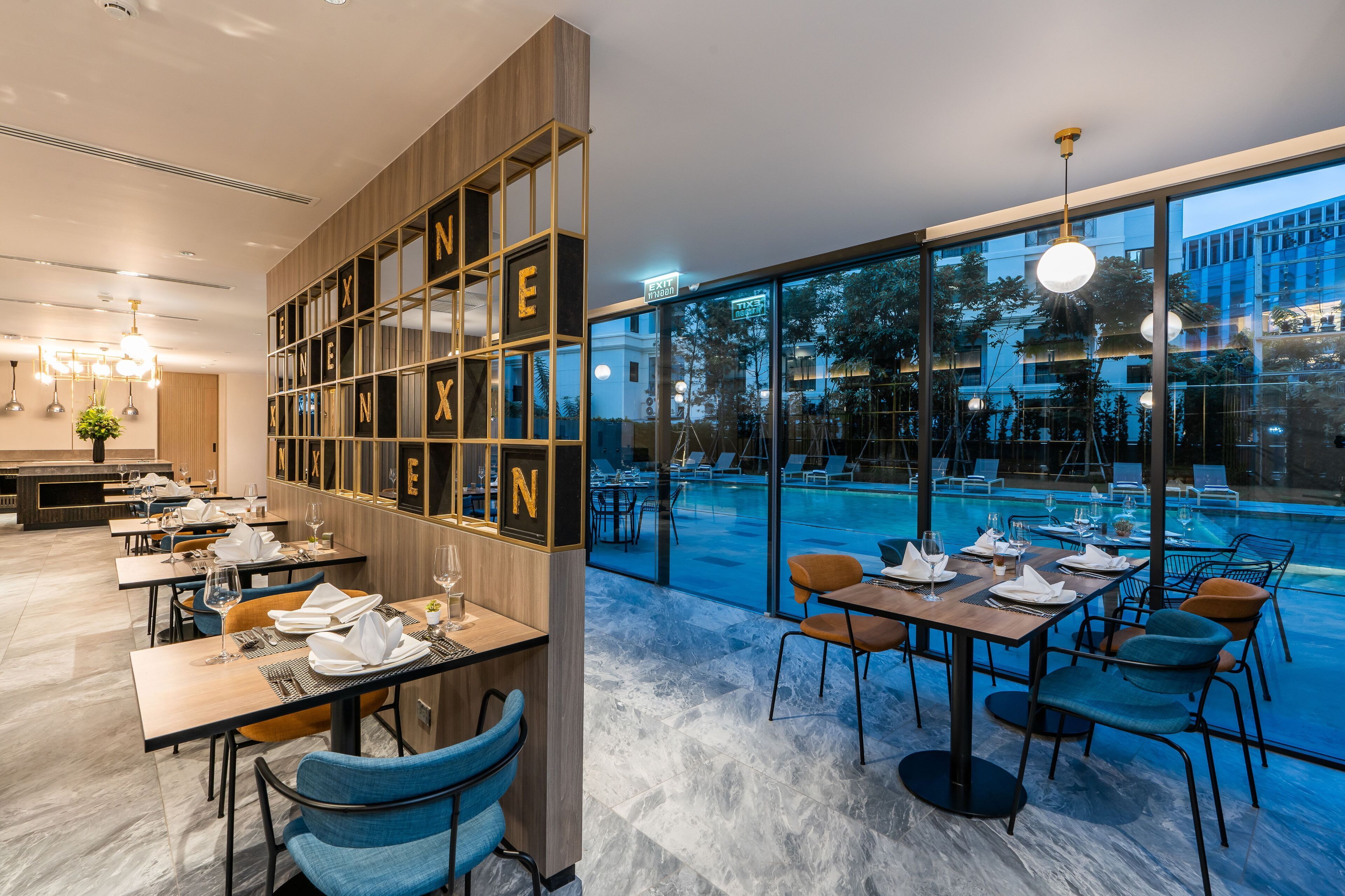 Ein modernes Restaurant mit Blick auf einen Pool, Marmorböden und einer Wand aus Holz mit Buchstaben.