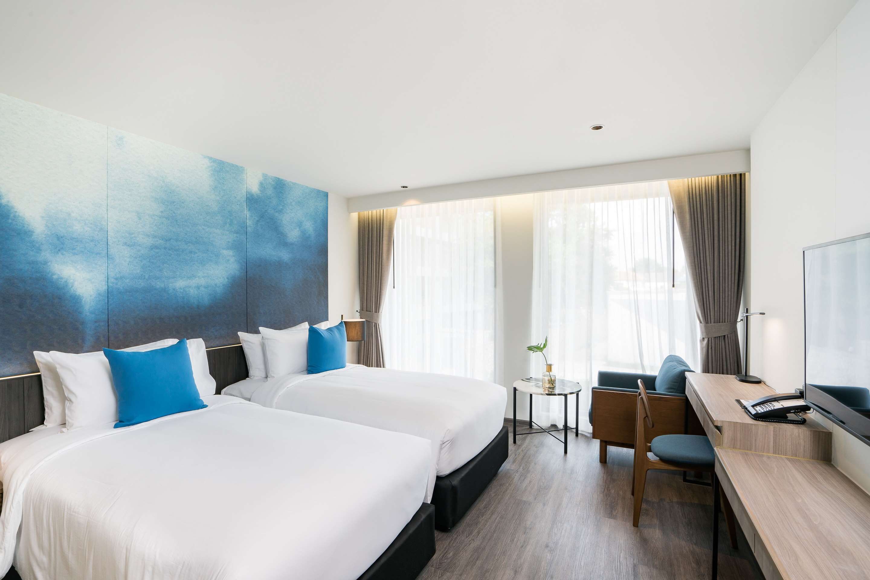 A hotel room with two beds, a desk, a chair, a TV, and a window with curtains.