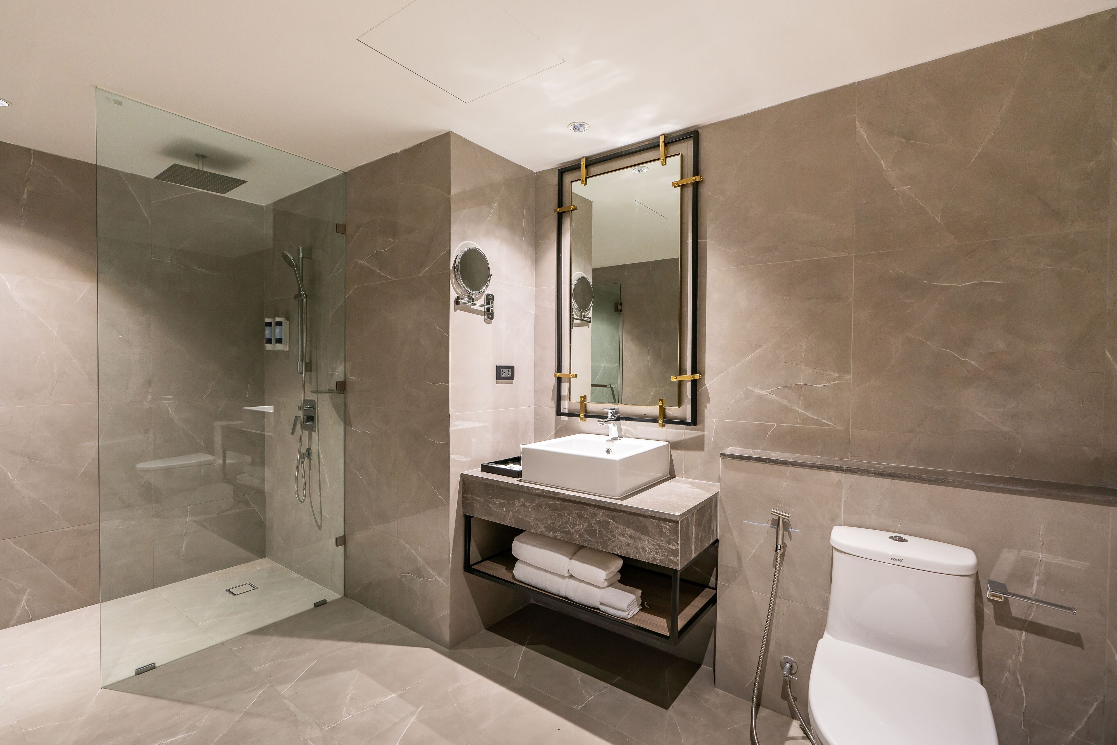 Un baño moderno con ducha envuelta en vidrio, tocador con lavamanos y retrete.