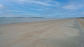 Uma extensa praia de areia com mar calmo e céu claro.