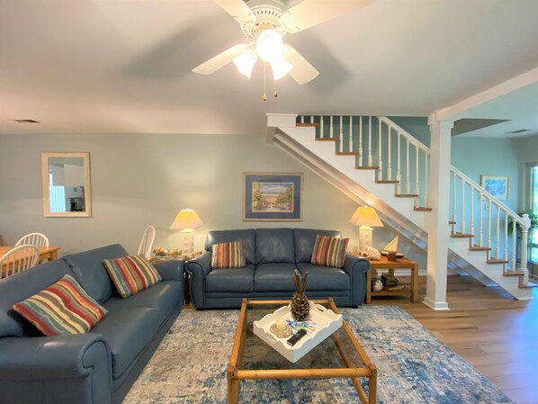 A living room with a blue sofa, a coffee table, a ceiling fan, and a staircase.