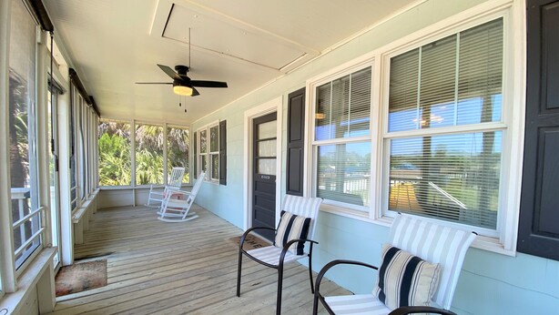 A covered porch with wooden flooring, white rocking chairs, and striped cushions. - Pet Friendly Cottage w/ Screened Porch & Easy Beach Access: WiFi Access (Edisto Beach)