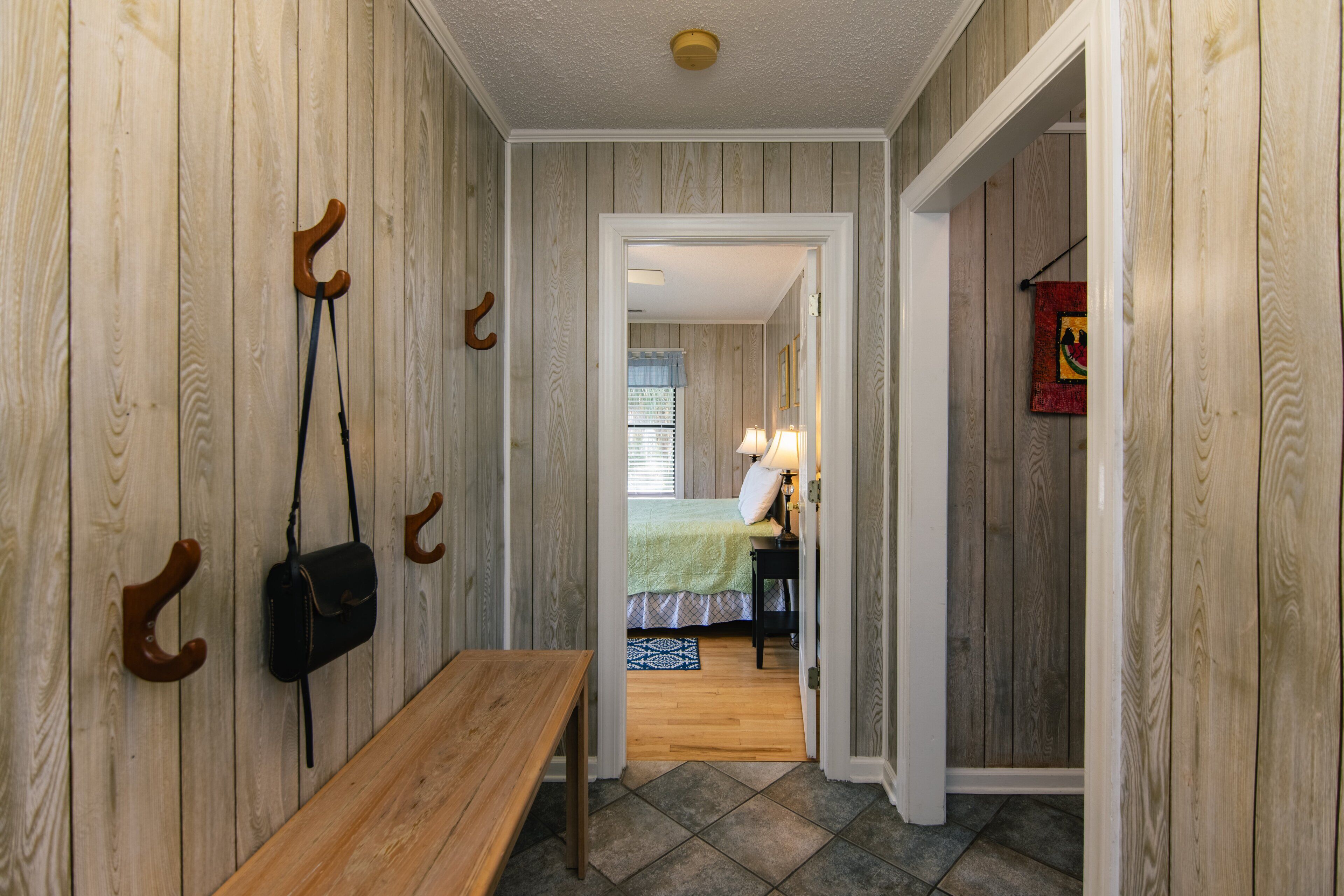 Un couloir avec des lambris en bois, un banc et un porte-manteau sur lequel est posé un sac.