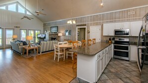 Una cocina amplia con una isla grande, comedor con sillas y sala de estar con sofá y televisor.