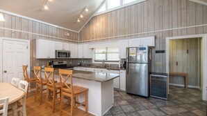 Una cocina con isla central, armarios blancos, refrigerador de acero inoxidable y un comedor con sillas de madera.