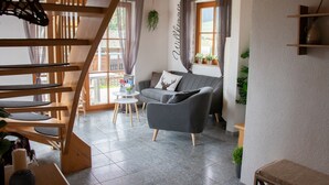 A modern living room with a grey sofa, a wooden staircase, and a view of the outdoors. - Ferienhaus Rudenberg (Titisee-Neustadt)