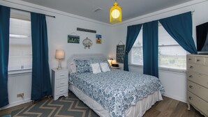 A bedroom with a bed, nightstand, dresser, and a hanging light fixture.