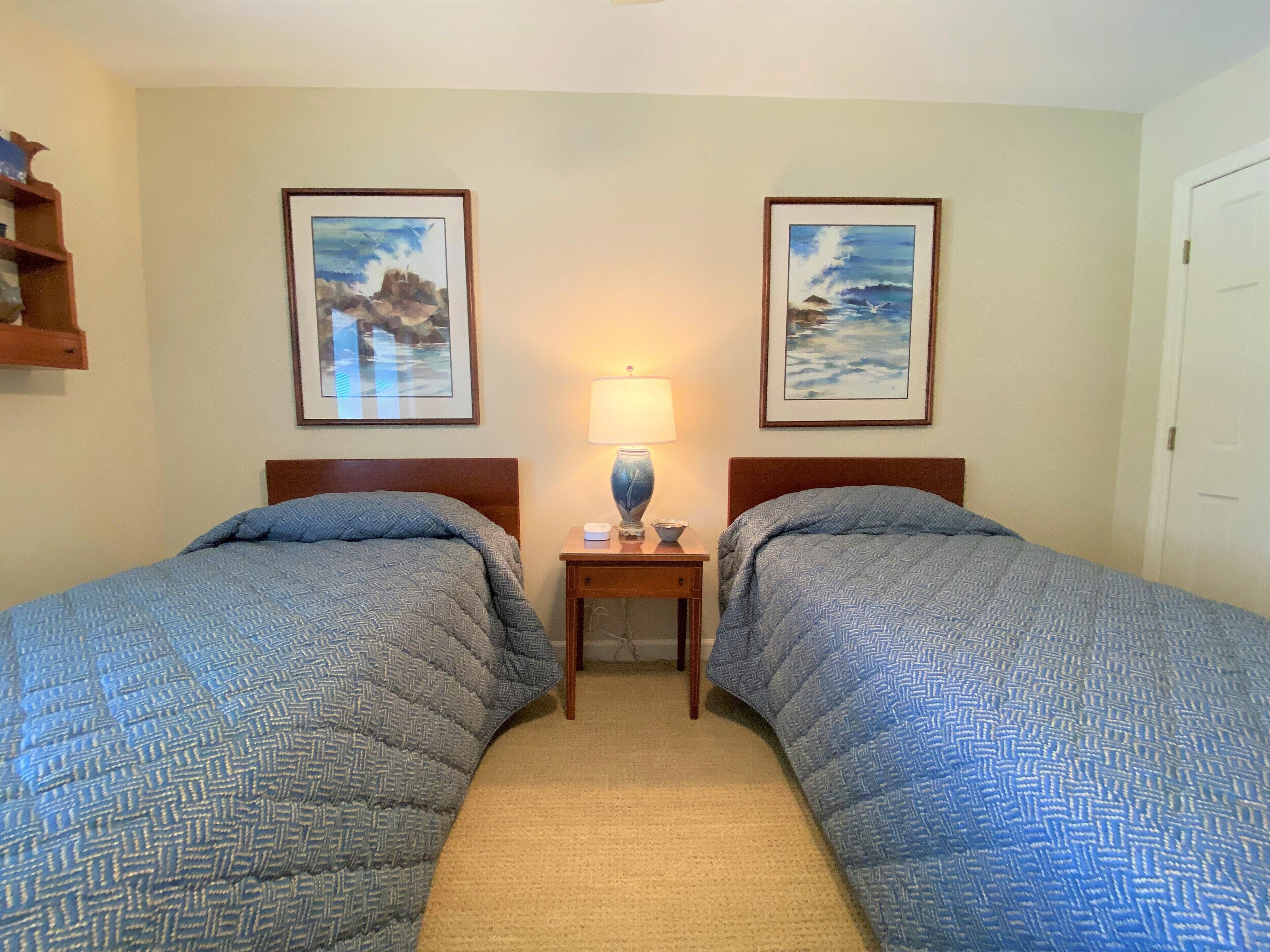 A hotel room with two beds, a nightstand with a lamp, and two framed pictures on the wall.