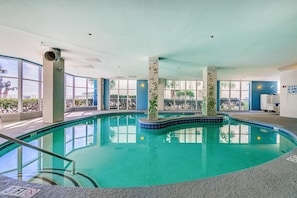 Una piscina interior con paredes de vidrio transparente, ventanas amplias y suelo de baldosas.