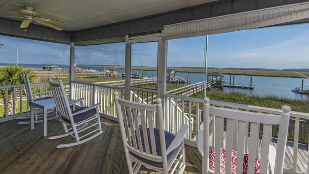 A covered deck with rocking chairs and a view of a marina.