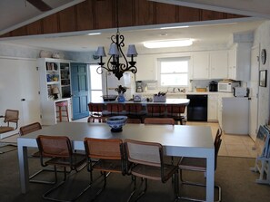 A modern kitchen with a central island, white cabinetry, and a dining area with wicker chairs.