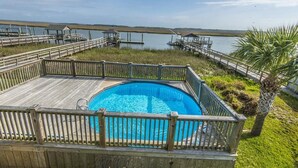 A wooden deck with a swimming pool, surrounded by a wooden fence and palm trees.