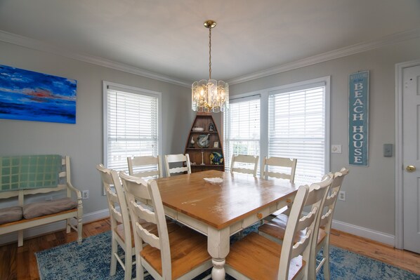 A dining room with a wooden table, white chairs, a chandelier, and a bookshelf.