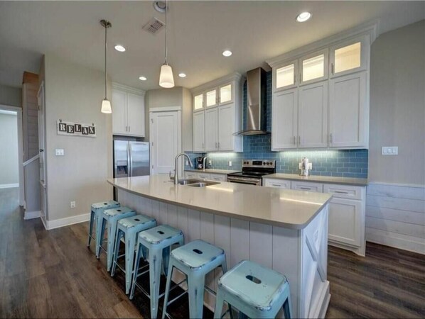 A modern kitchen with white cabinets, a large island with bar stools, and a blue backsplash.